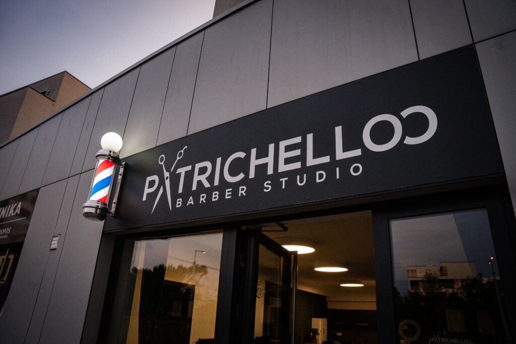 Detail loga Patrichelloo Barber Studio a barber pole na fasádě budovy